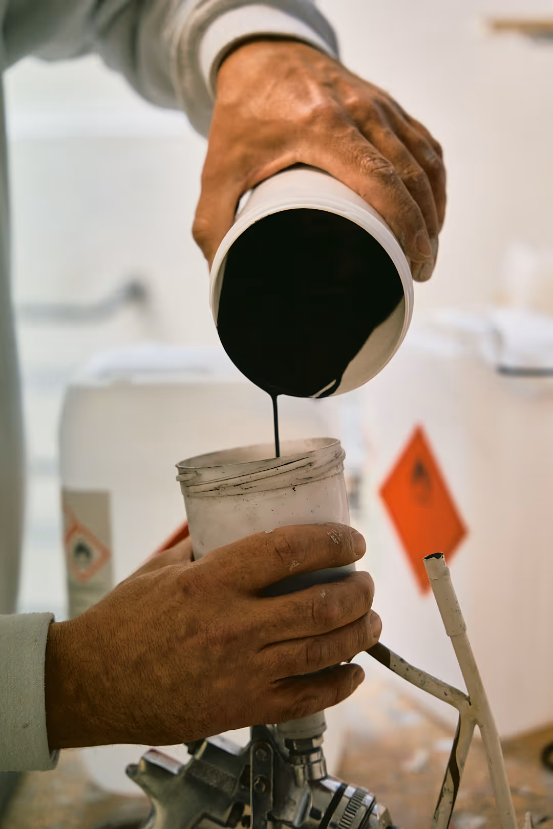 Hände giessen schwarze Farbe aus einem Becher in die Behälterkammer einer Lackierpistole.