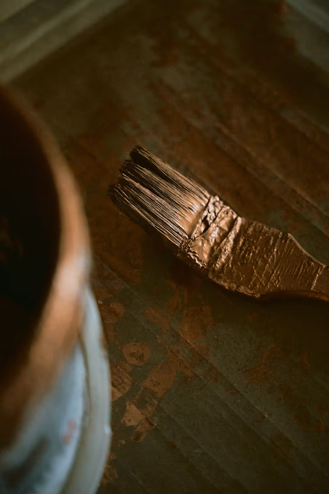 Nahaufnahme eines breiten Pinsels mit brauner Farbe auf einer dunklen Oberfläche.