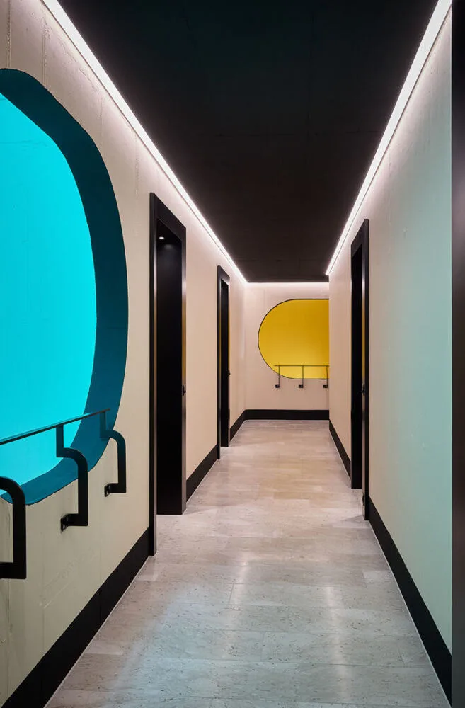 Moderner Flur mit schwarzen Türen, einem schwarzen Deckenspiegel und runden Fenstern mit blauem und gelbem Hintergrund.
