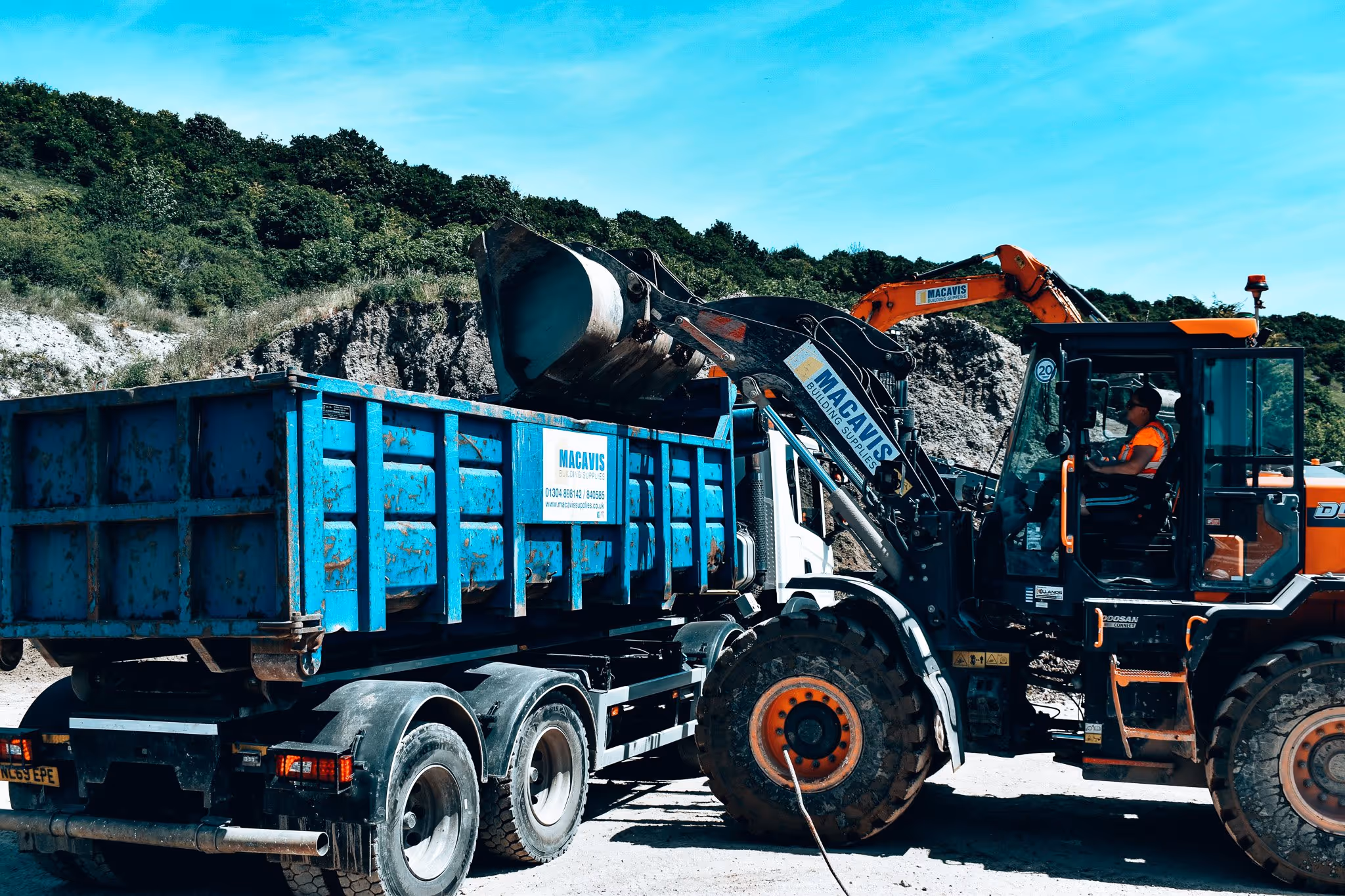 Blue industrial truck and loader working at rocky construction site