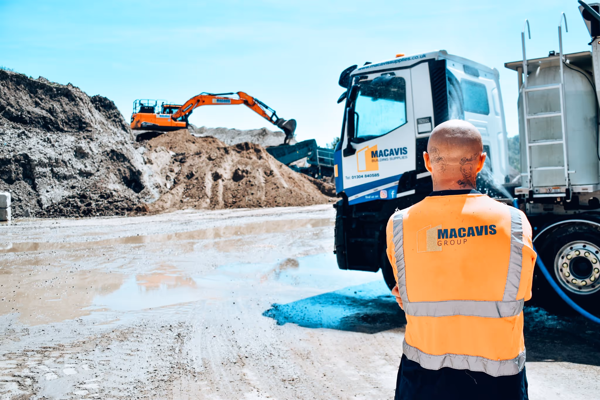 Worker in high-visibility vest at construction site with excavator and truck