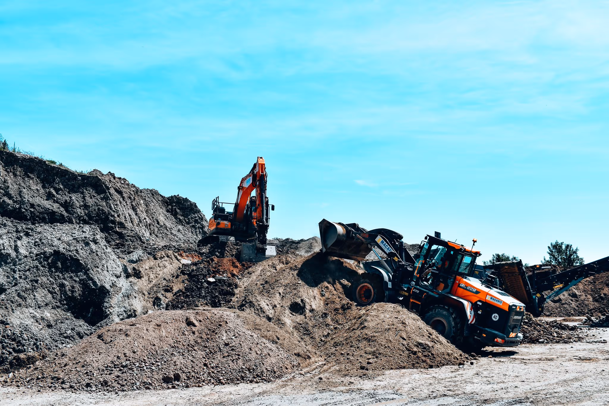 Construction vehicles excavating dirt at industrial site under blue sky