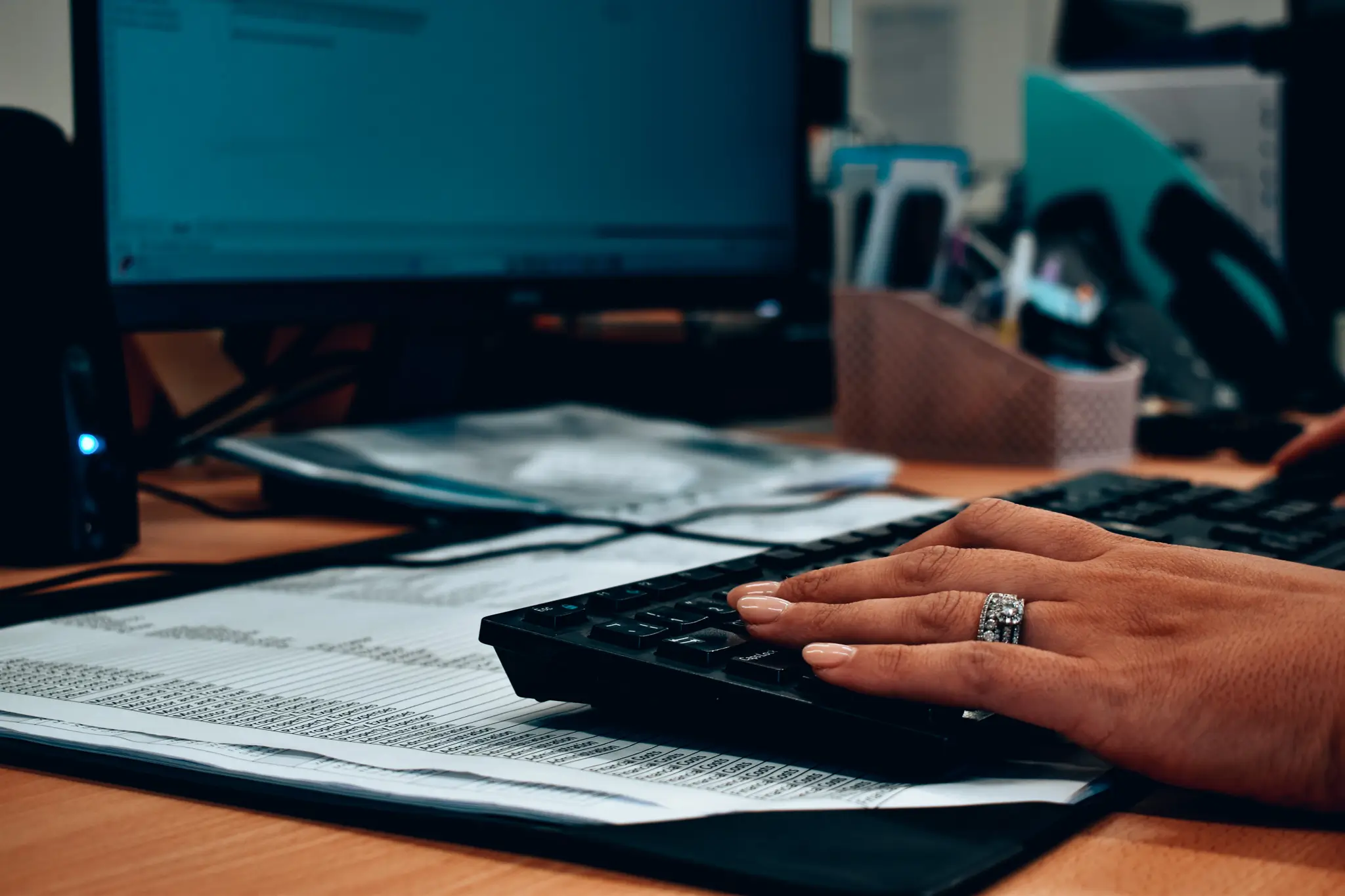 Hand on keyboard near computer screen with documents and office supplies