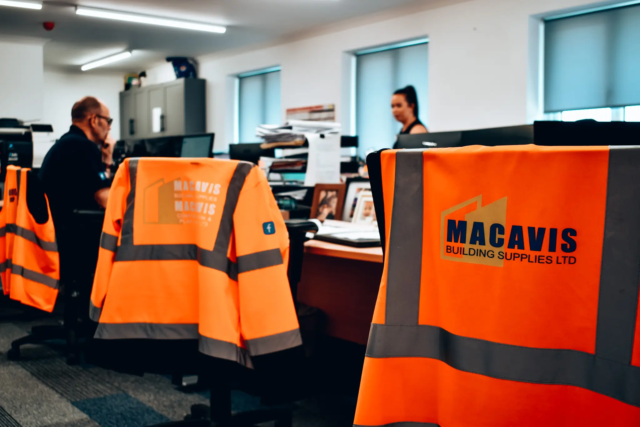Bright orange Macavis Building Supplies safety vests in office workspace