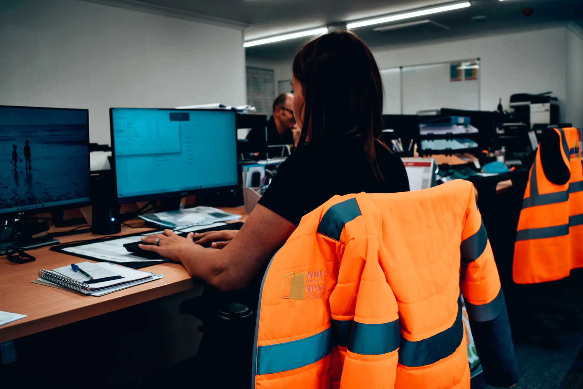 Worker in orange safety vest working at computer in office workspace