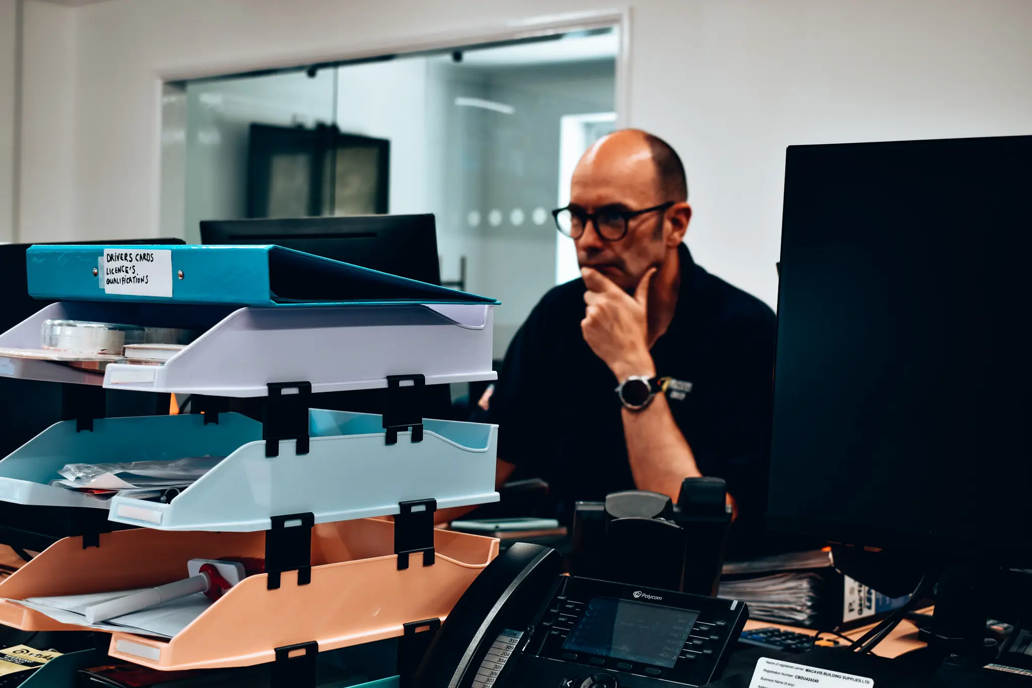 Office worker looking thoughtful near stacked document trays and computer