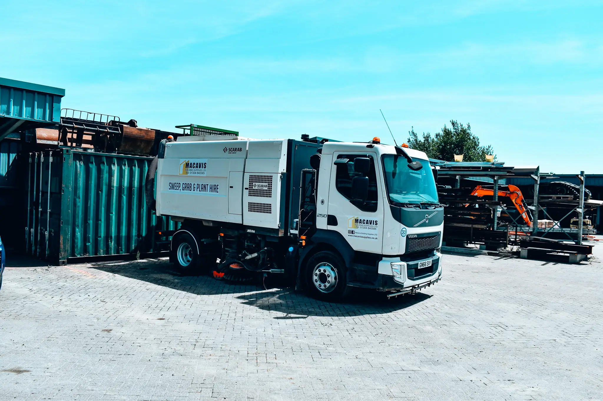 White street sweeper truck parked near shipping containers on paved lot