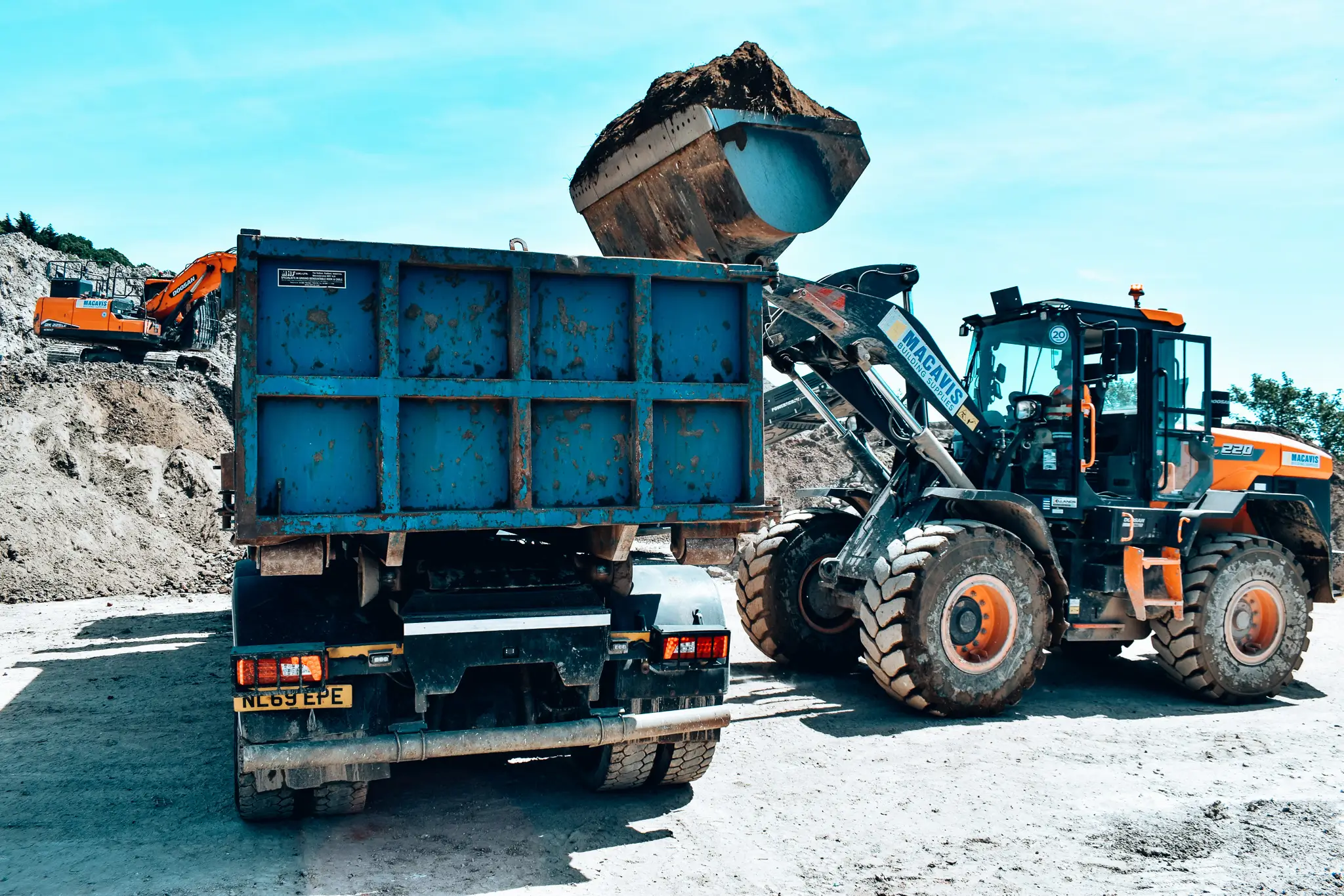 Wheel loader dumping dirt into blue container at construction site