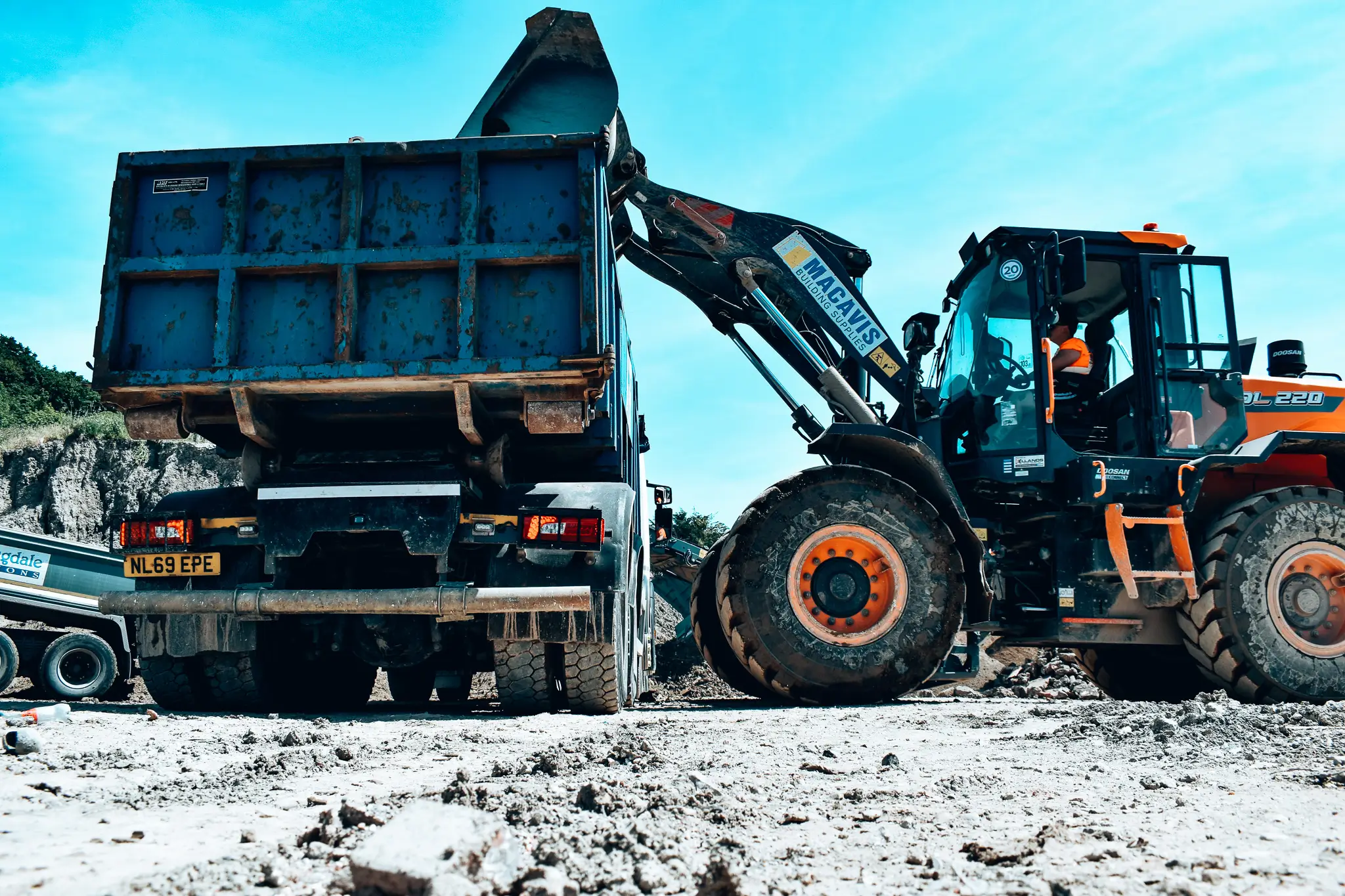 Heavy machinery loading blue dump truck at construction site