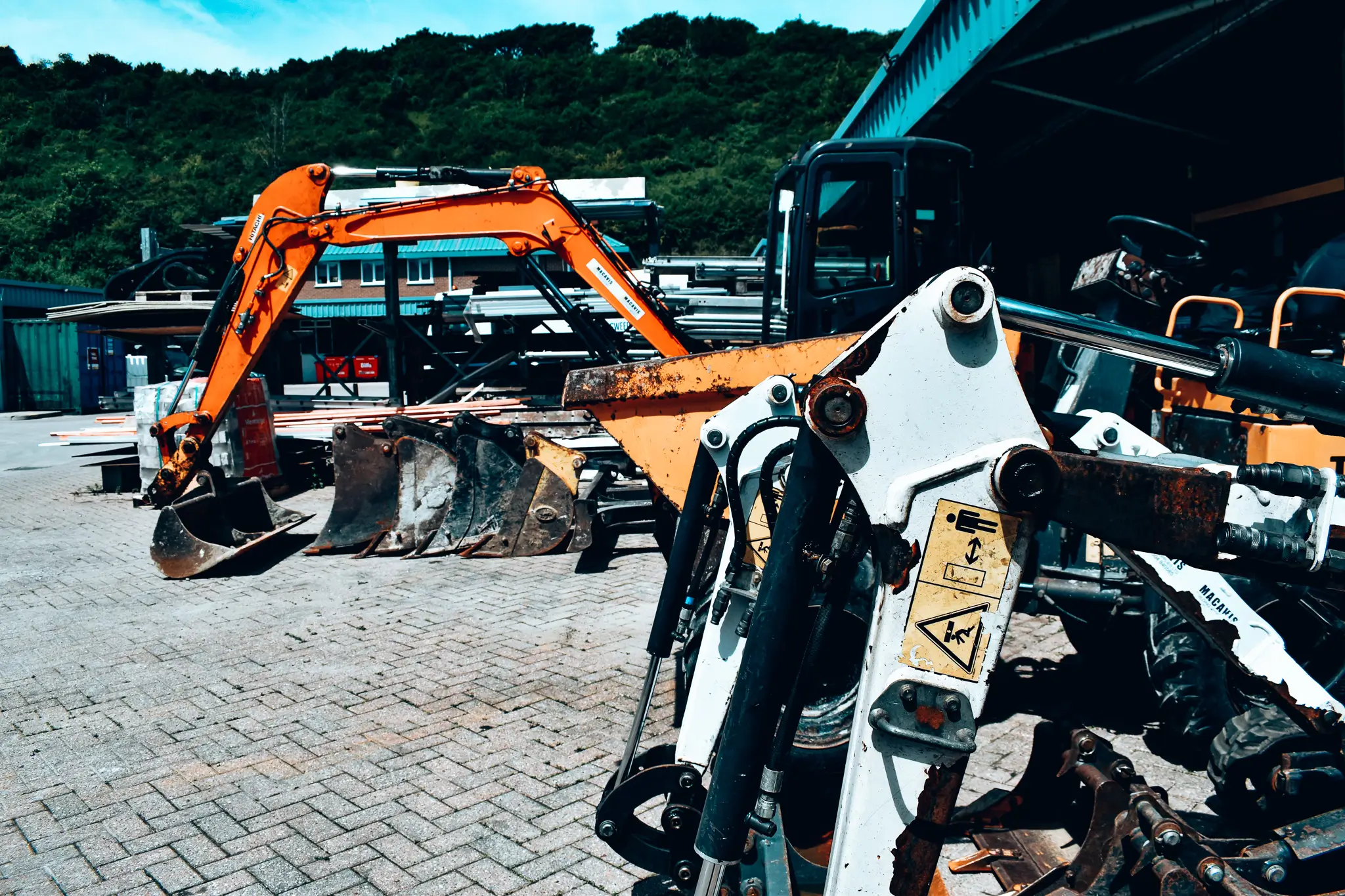 Construction excavators parked on brick pavement with forest in background