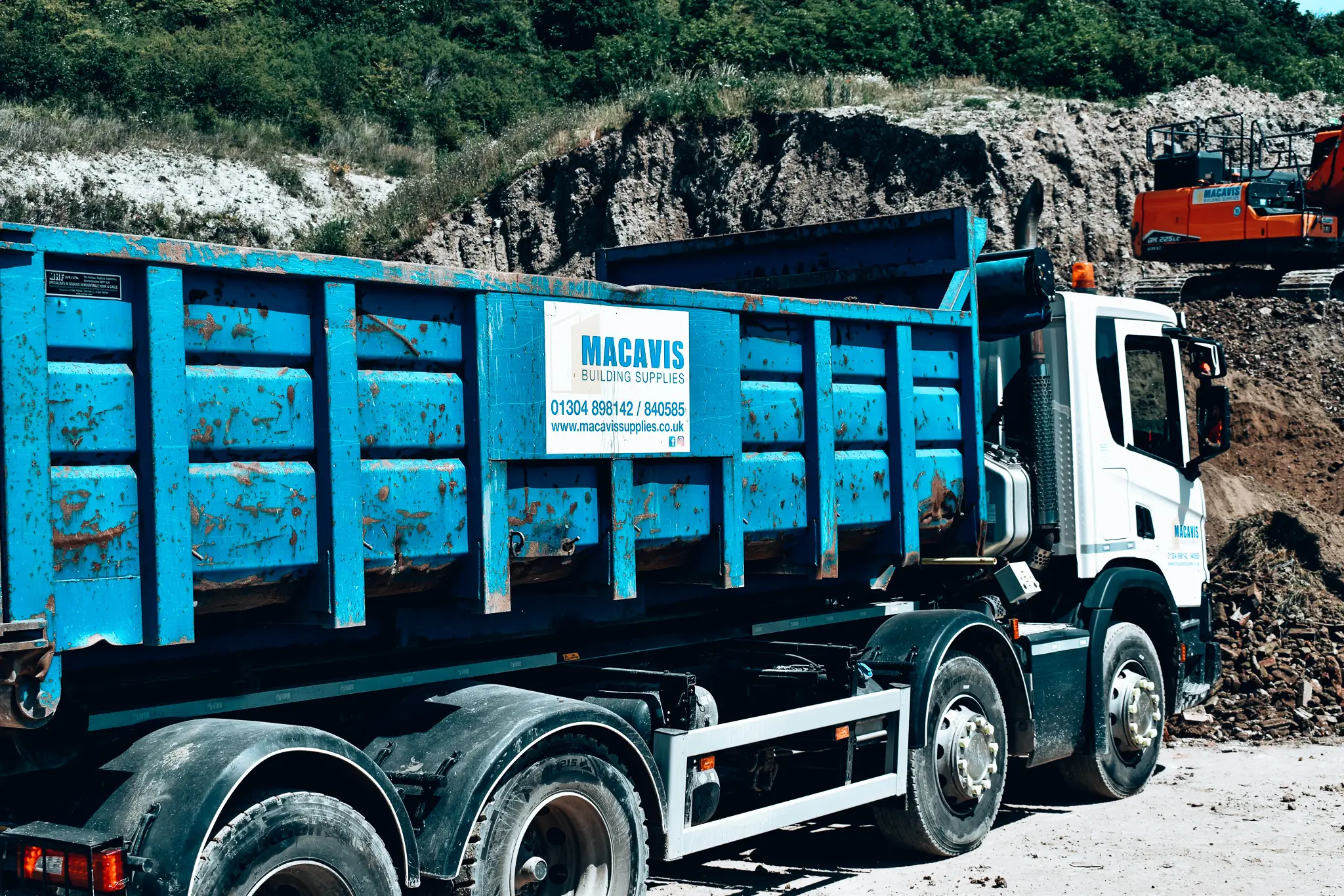 Blue Macavis building supplies truck parked at construction site with rubble