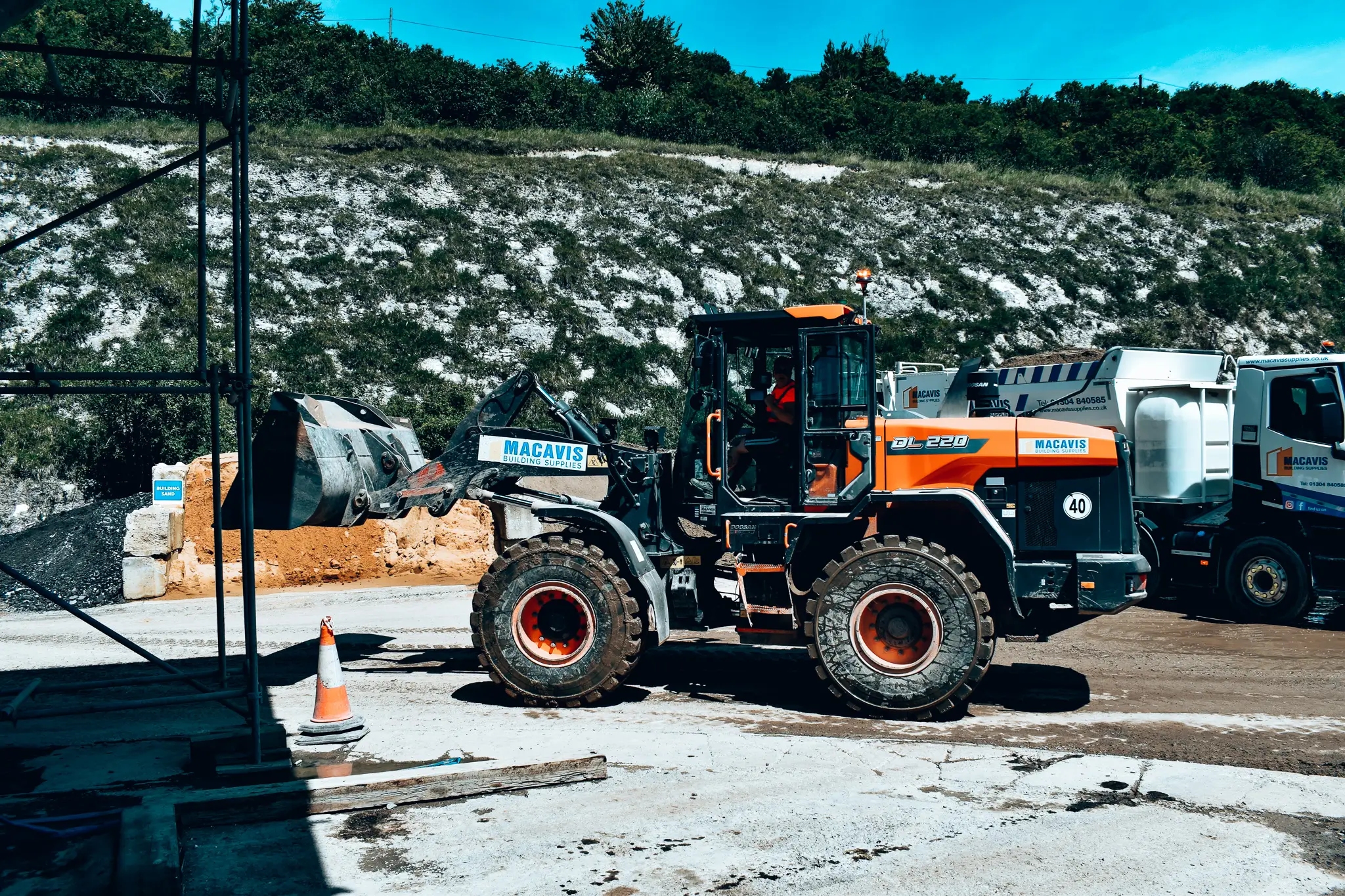 Orange Macavis construction loader at quarry site with trucks and rocky background