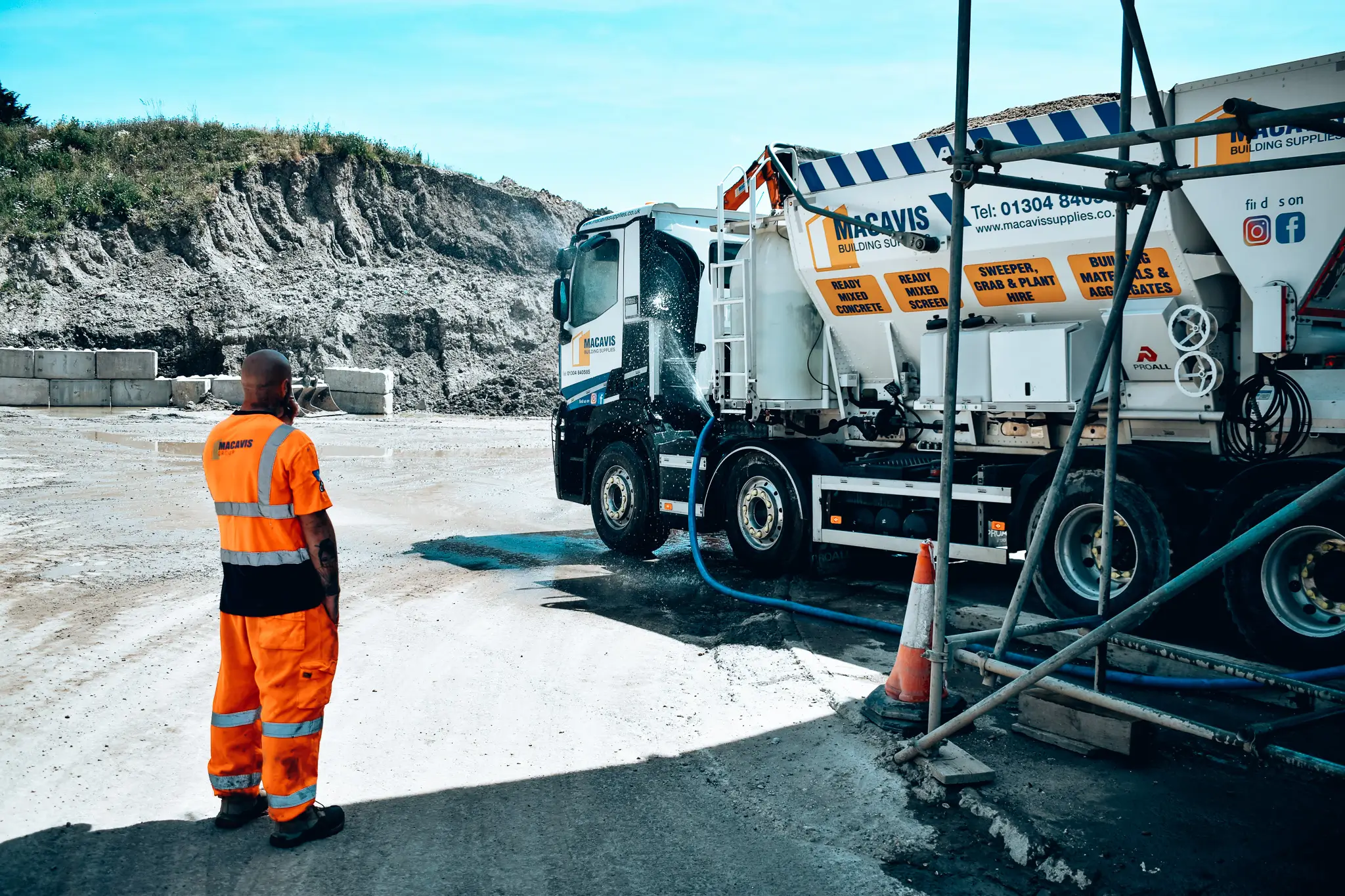 Worker in orange safety gear standing near Macavis construction truck at quarry site