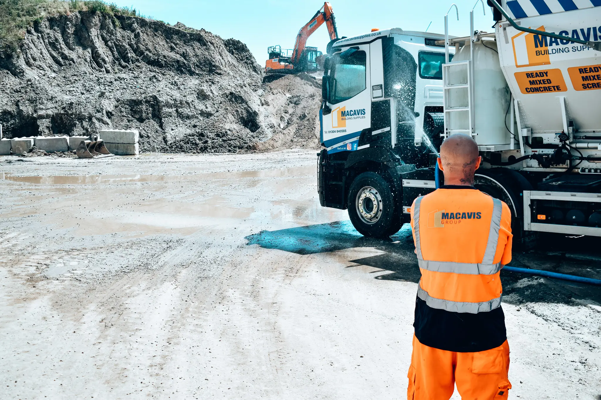 Macavis worker in orange vest standing near concrete mixer truck at construction site