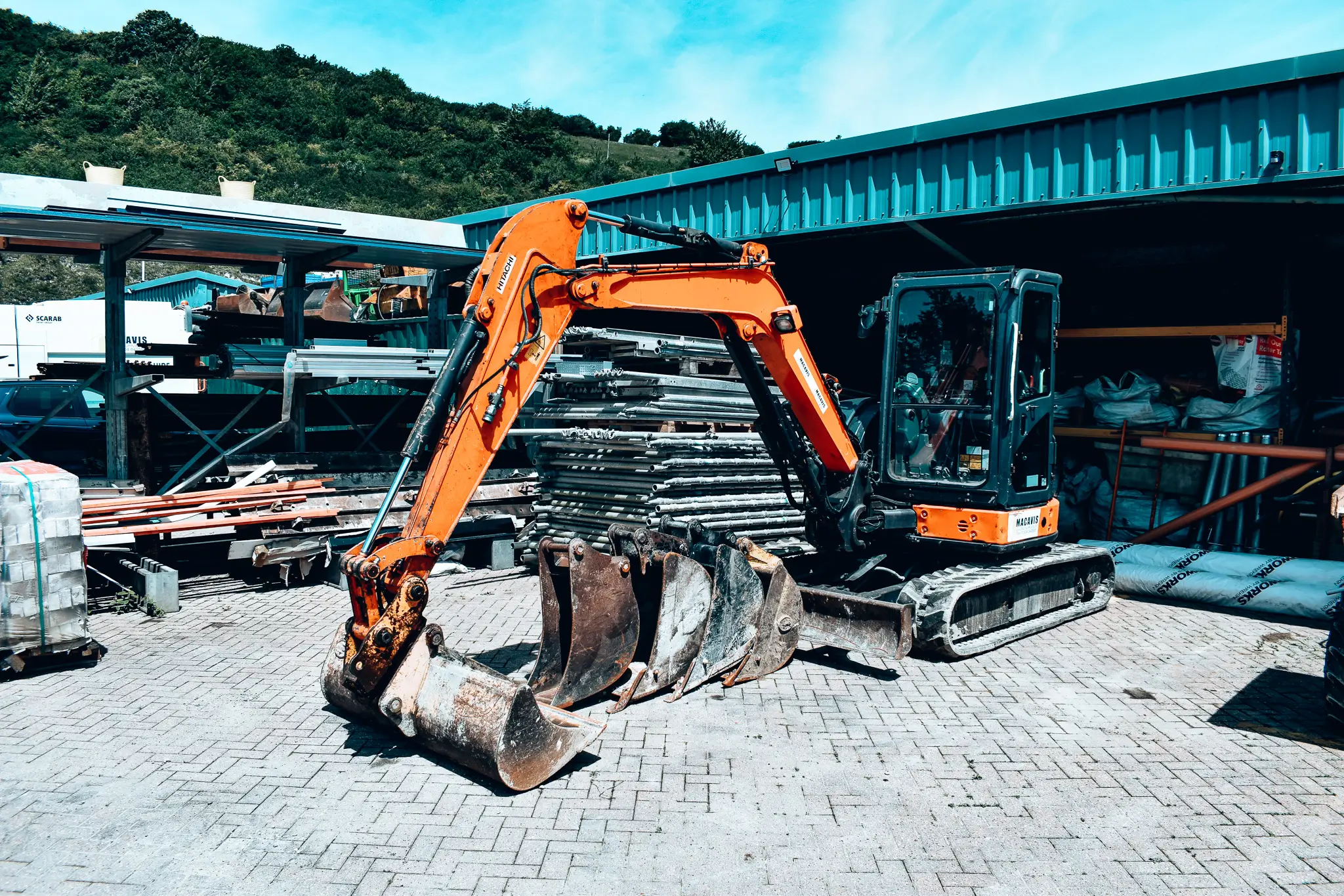Orange excavator with large bucket on brick pavement near industrial building