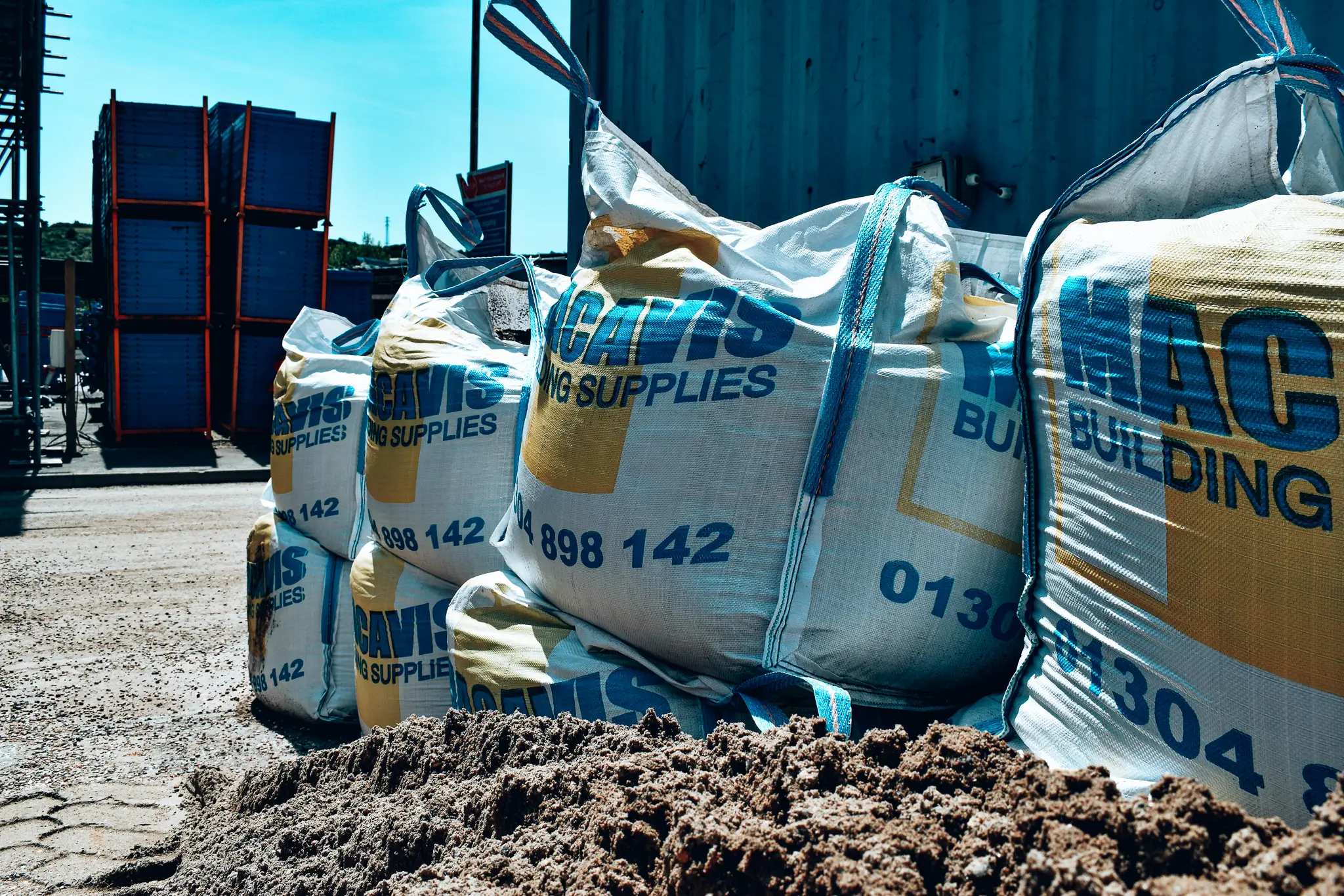 Large white and blue building supply bags stacked on dirt at construction site