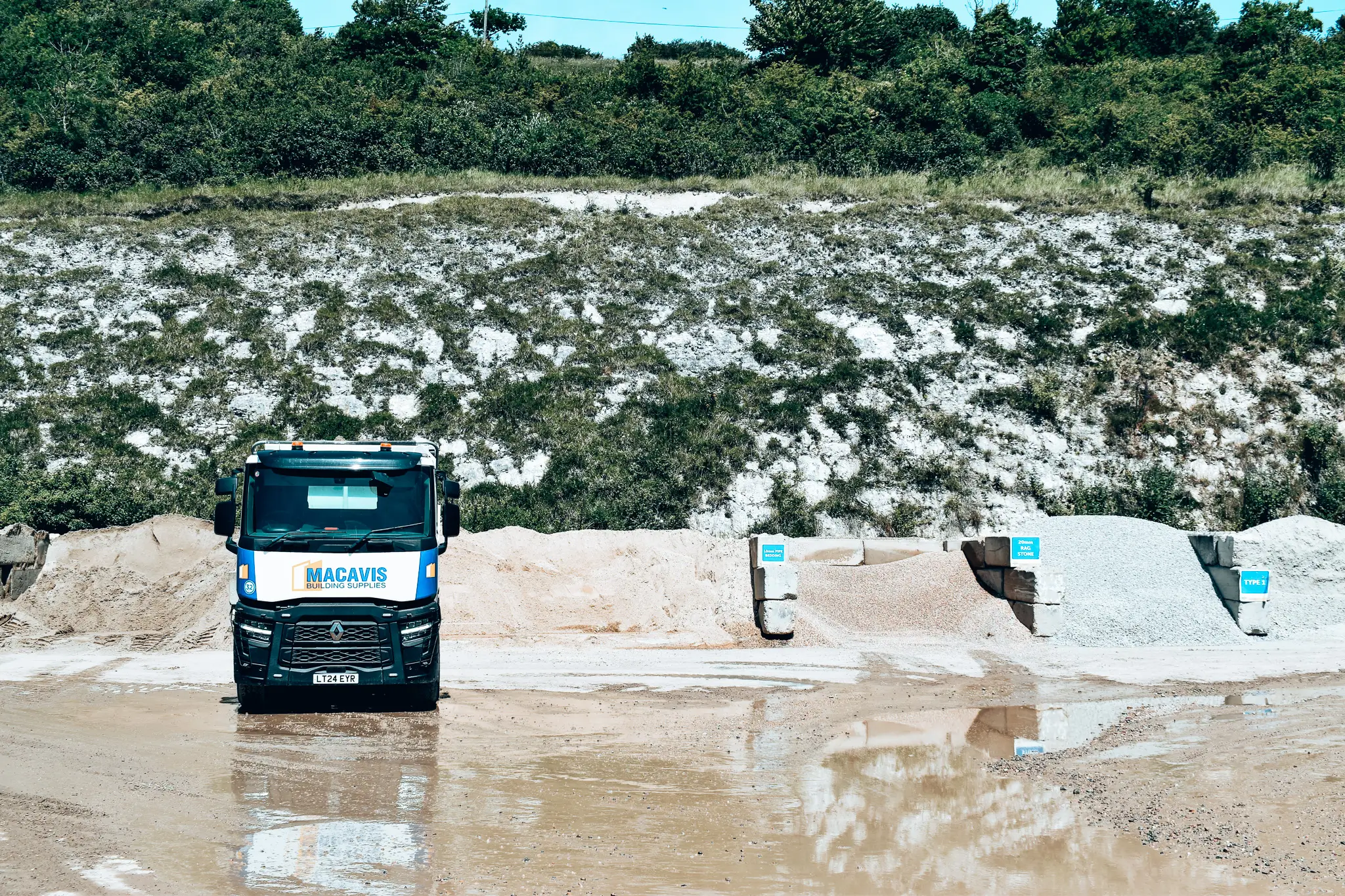 Macavis building supplies truck parked at muddy construction site with sand piles