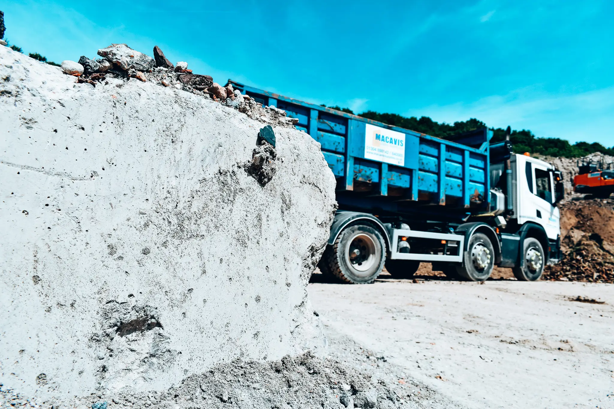 Blue Macavis dump truck at construction site with large white rock