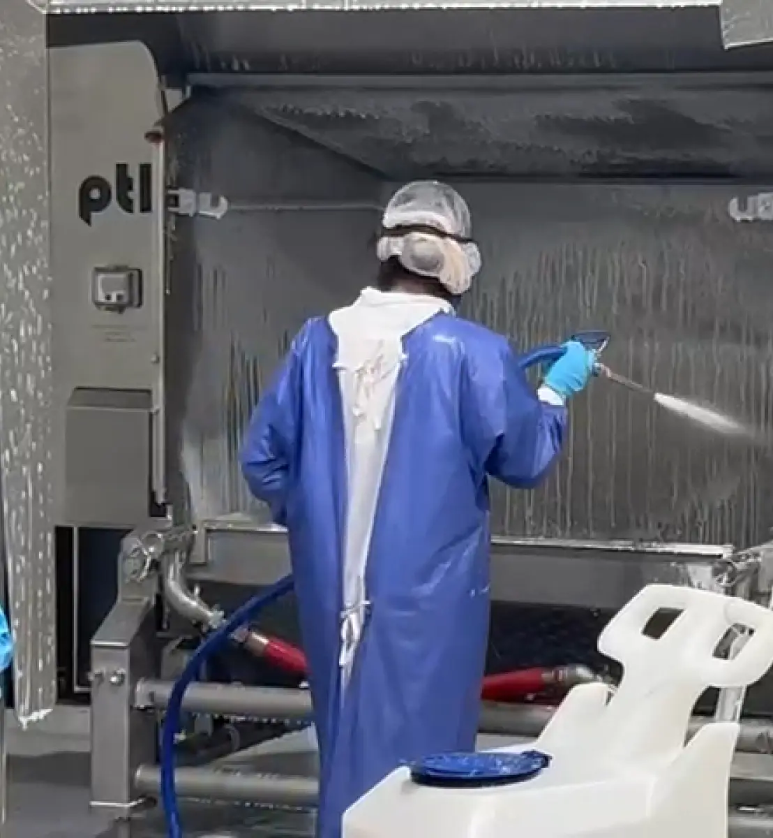 A man wearing a blue suit and a mask is spraying a surface with a hose.