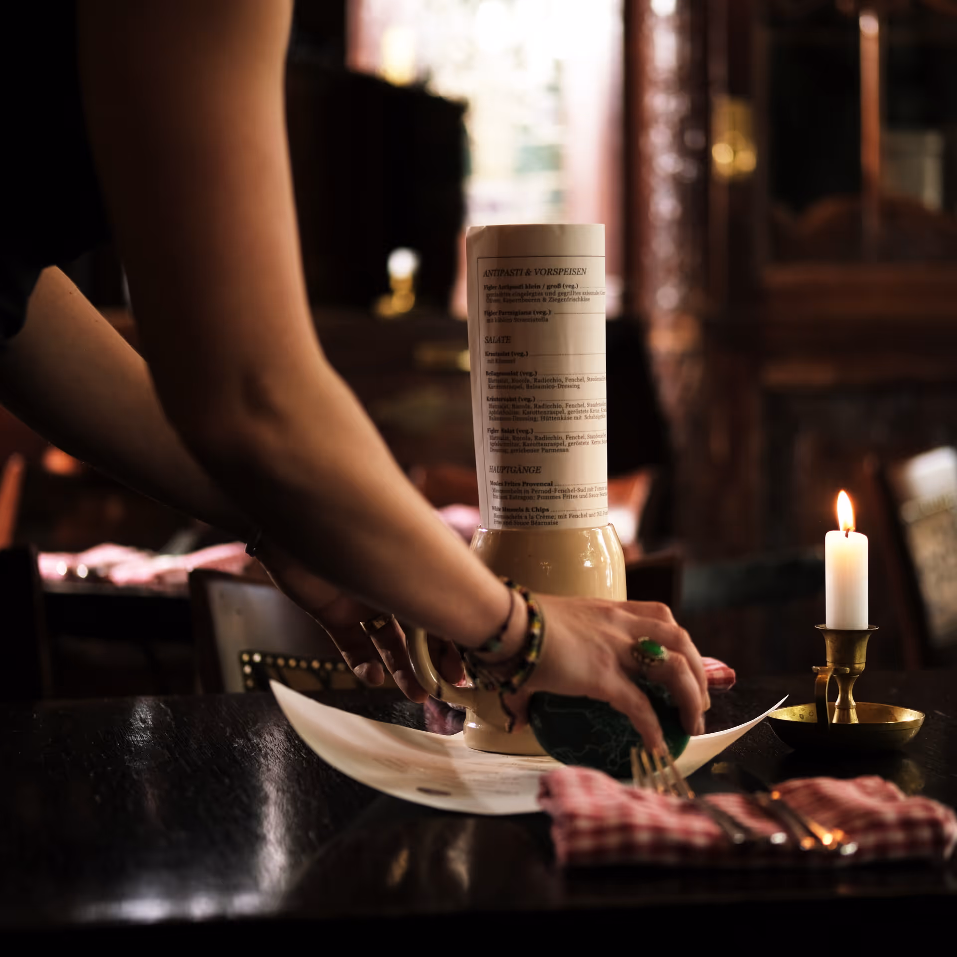 Person deckt einen Tisch im Restaurant mit Speisekarte und Besteck.