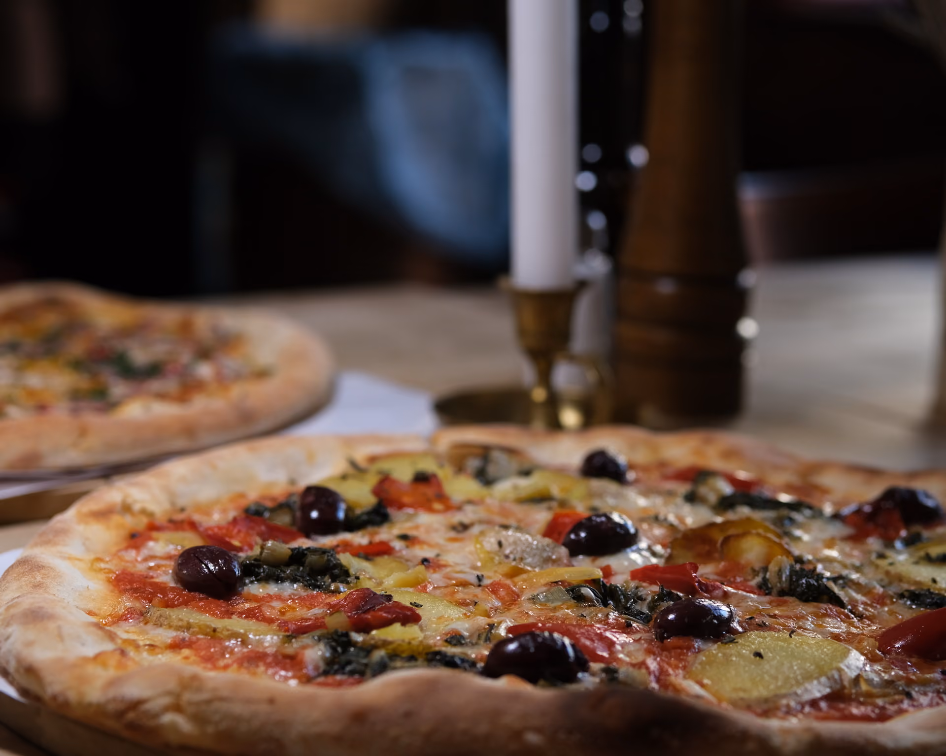 Person hält eine frisch gebackene Pizza mit Hackfleisch und Käse auf einem Pizzaschieber.