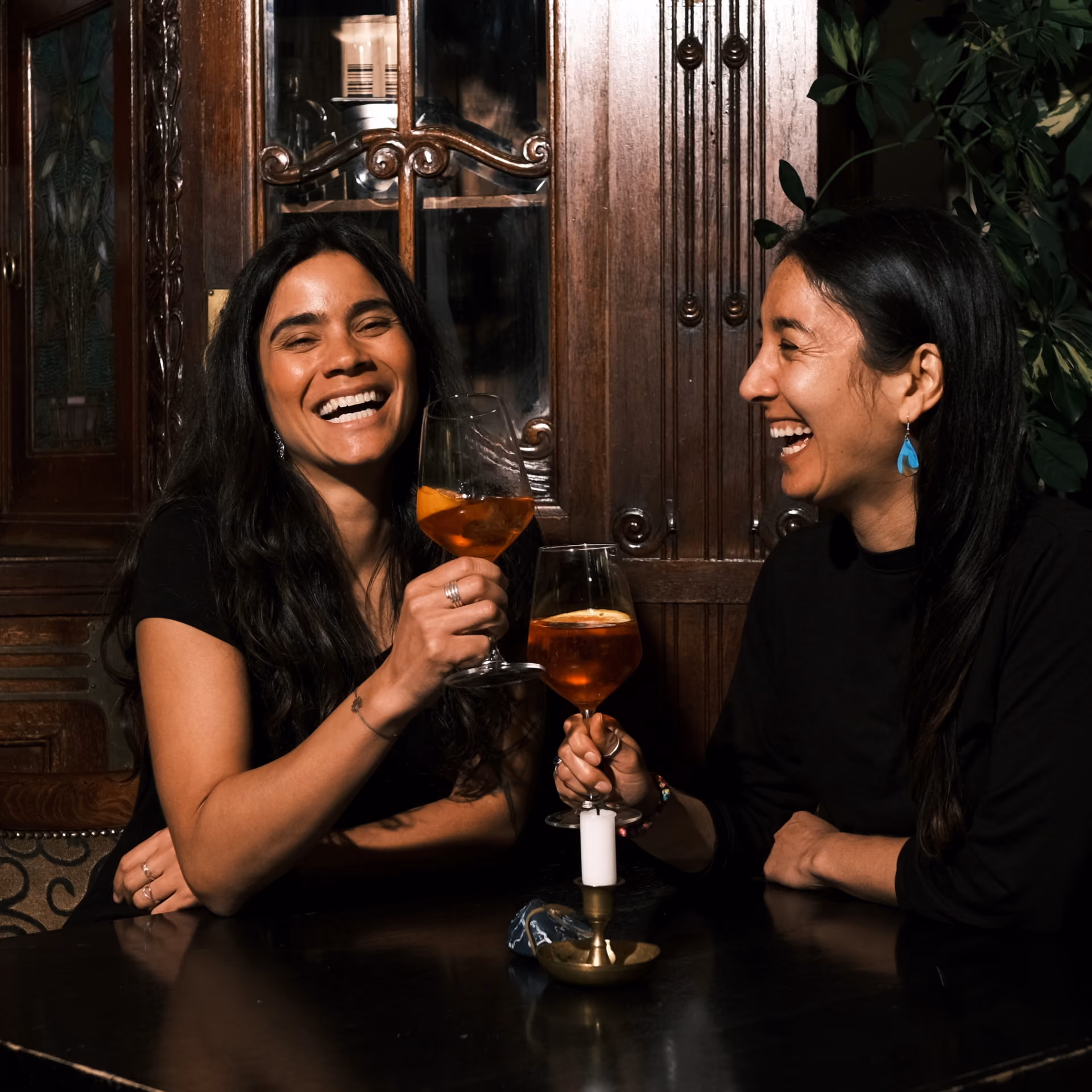 Zwei Frauen lachen und stoßen mit einem Aperitif in einem gemütlichen Restaurant an.