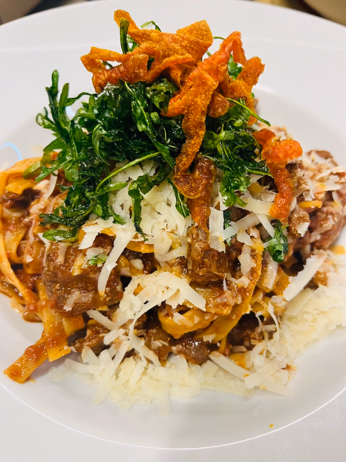 Teller mit Bandnudeln, Wildschweinragout, geriebenem Käse und frischen Kräutern.