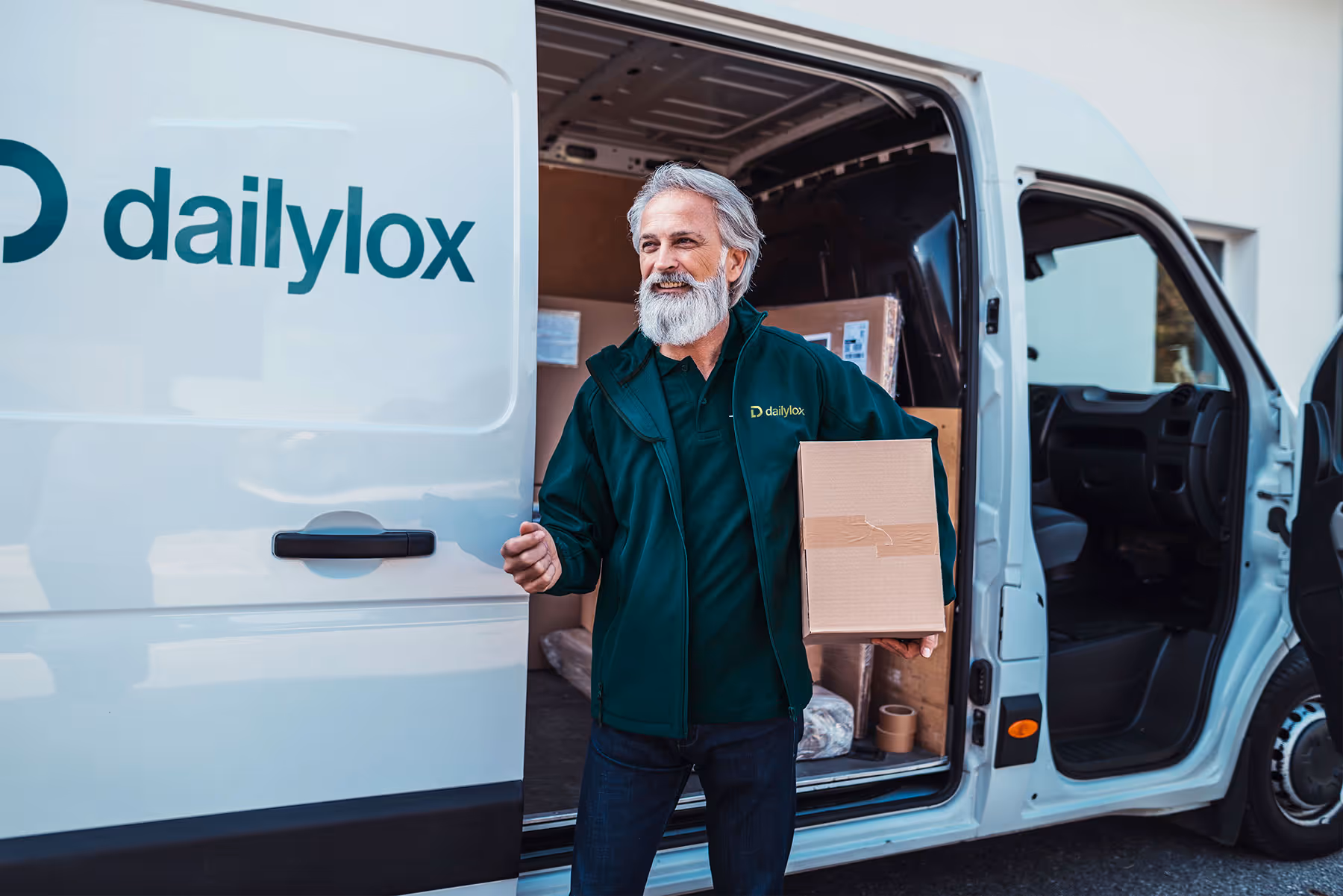 Ein freundlicher Paketbote von dailylox steigt aus einem Lieferwagen und trägt ein Paket. Der Transporter ist mit dem dailylox-Logo versehen. Im Hintergrund sind weitere Pakete im Fahrzeug sichtbar.