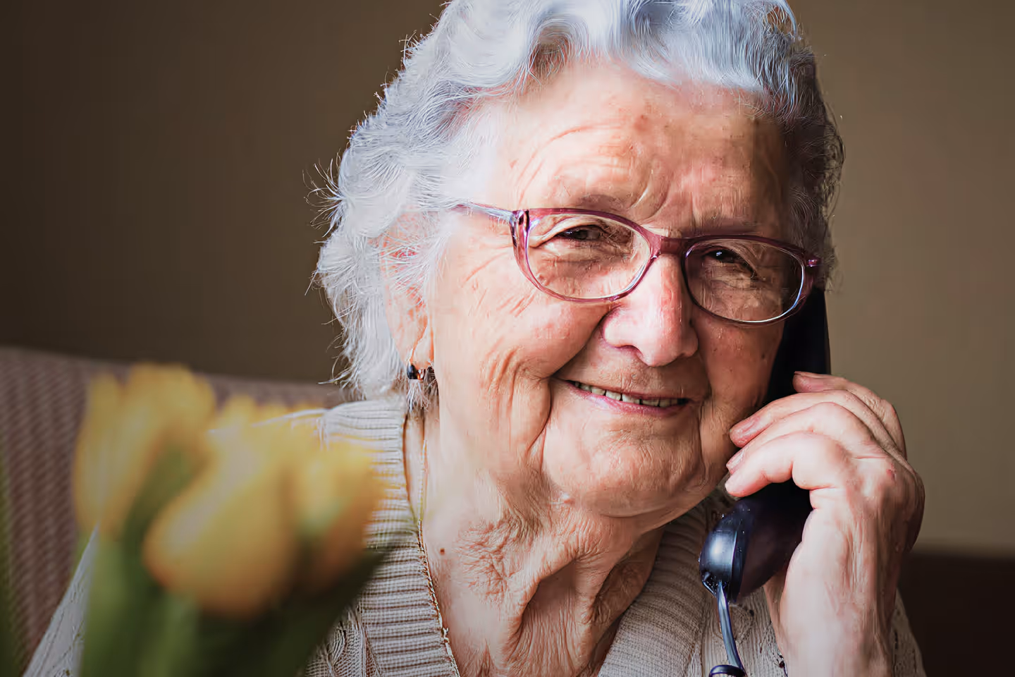 Smiling older woman with gray curly hair speaking on smartphone outdoors, wearing glasses – staying in touch with family