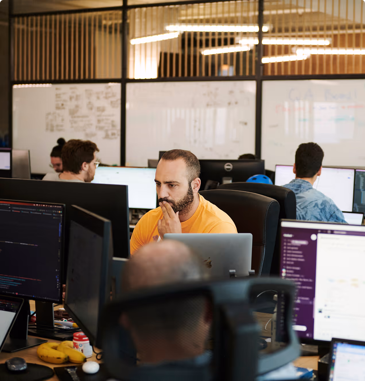 Mehrere konzentrierte Personen arbeiten an Computern in einem modernen Büro mit Glaswänden und Whiteboards.