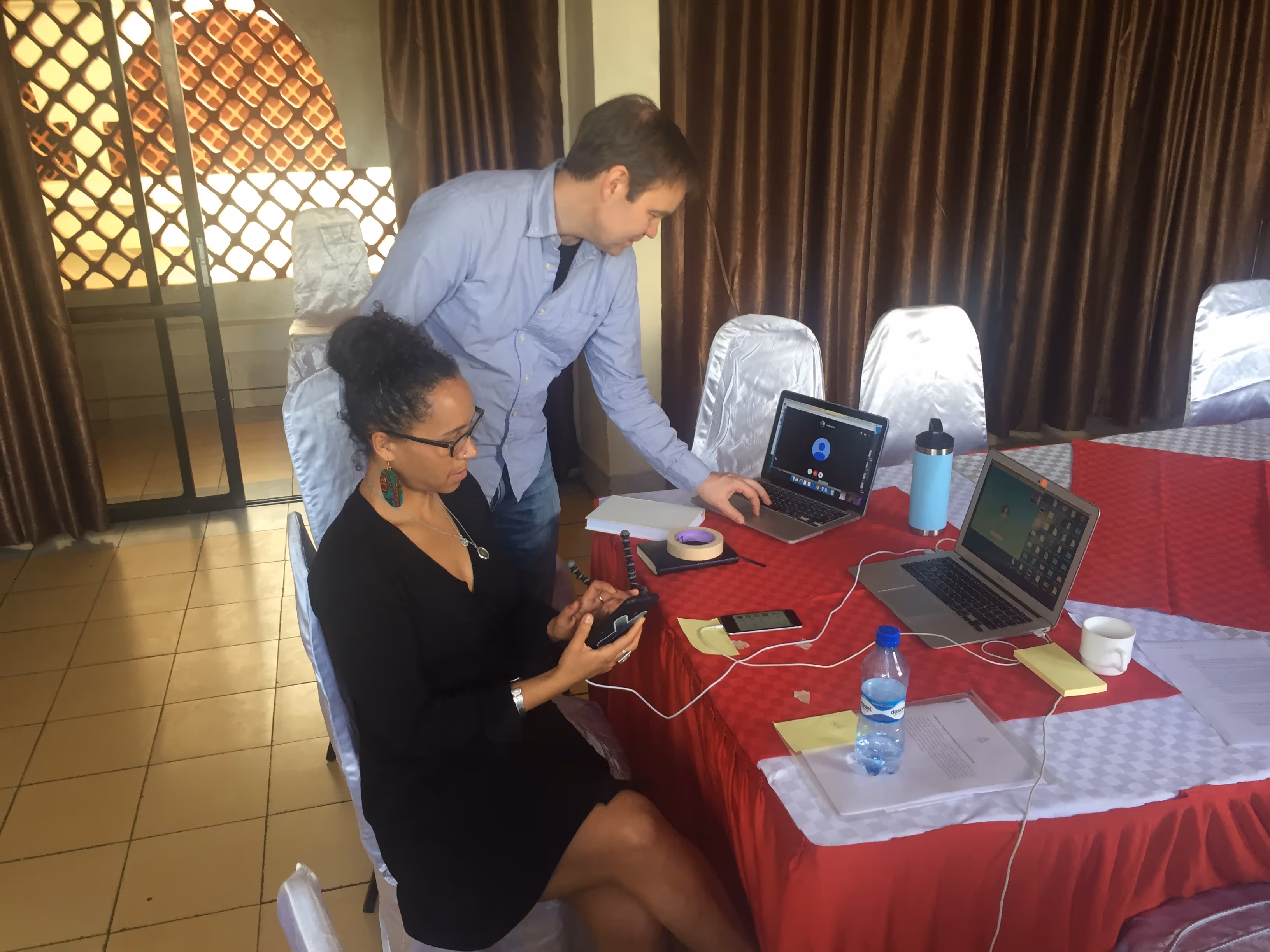 Foxfire's Founder, Dacia, is sitting at a table conferring with a colleague. There are multiple laptops on the table.