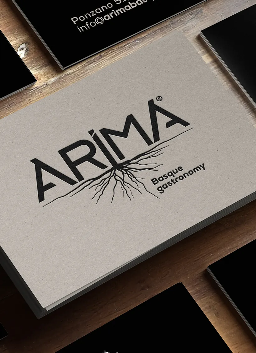 Tarjetas de presentación apiladas con el logo ARIMA y el texto Basque gastronomy, con diseño de raíces debajo del texto.