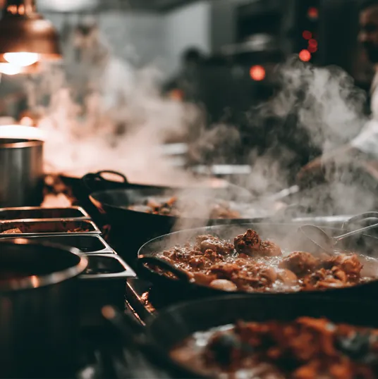 Sartén humeante con salsa y albóndigas cocinándose en una cocina profesional.