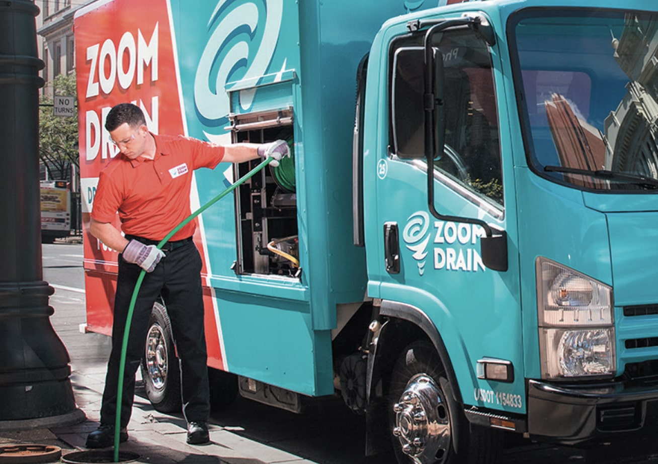 Zoom Drain service technician standing next to a teal company truck.