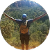Person standing in nature with hills and greenery in the background.