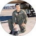 Man in military pilot uniform kneeling on a tarmac.