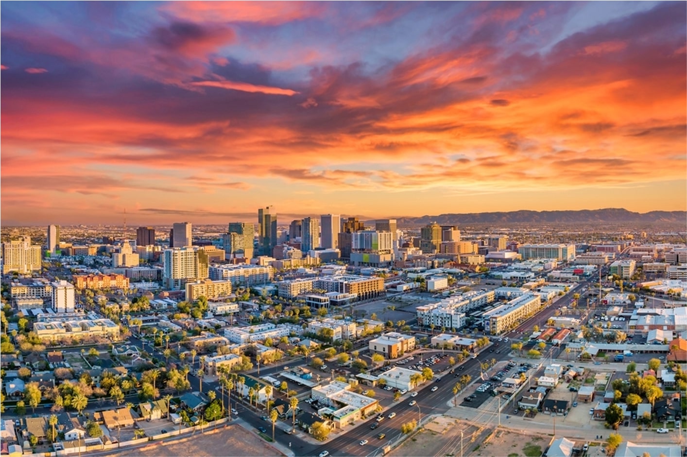 Aerial view of a city skyline at sunset with vibrant orange and pink clouds.