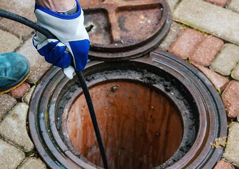 Worker operating drain cleaning equipment next to an open manhole.
