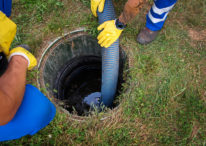 Worker in yellow gloves lowering a hose into a drain opening.