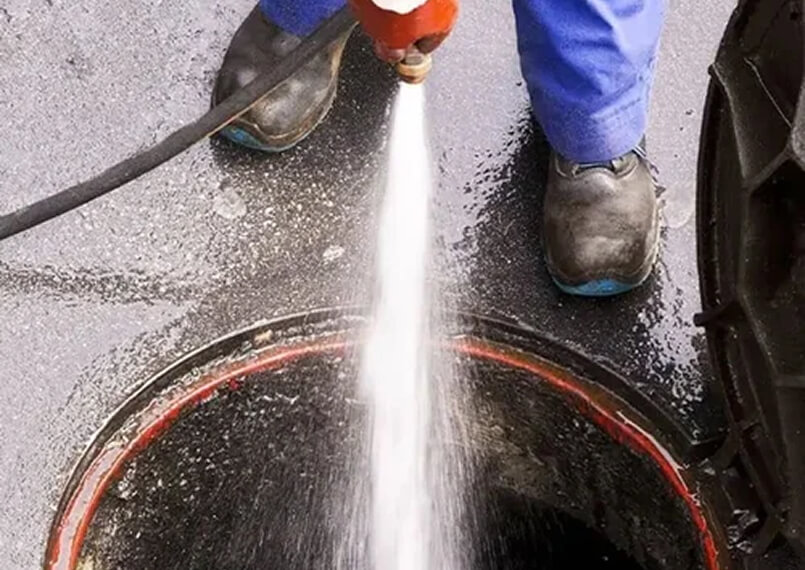 Worker using a high-pressure hose for drain cleaning.