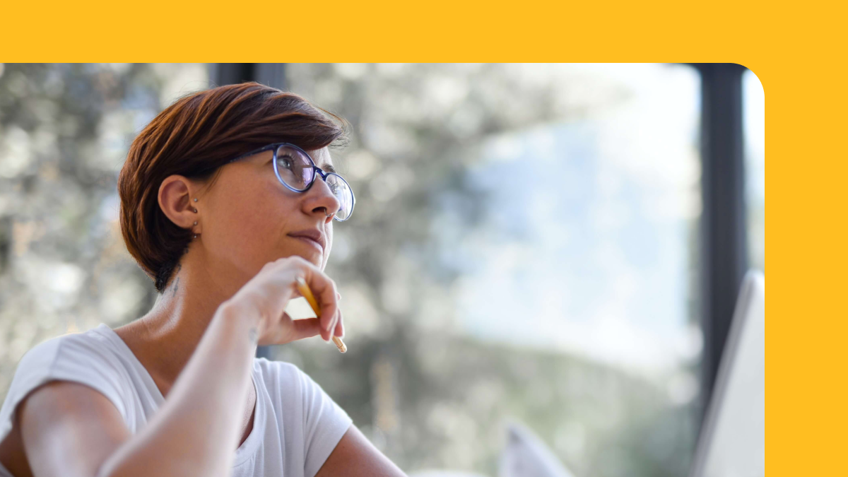 A woman looks thoughtfully up from their laptop