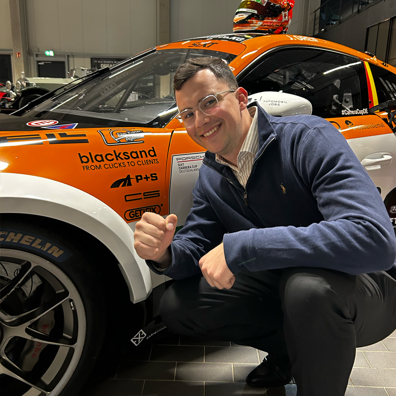 Eine Mann vor einem Porsche GT3 Cup Auto, welcher freundlich schaut.