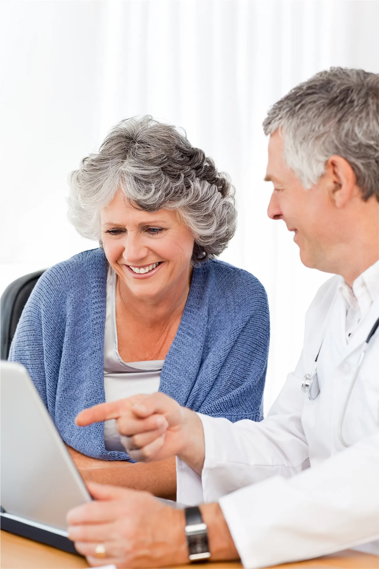 Senior woman smiling while discussing information on a laptop with a male doctor in a white coat.