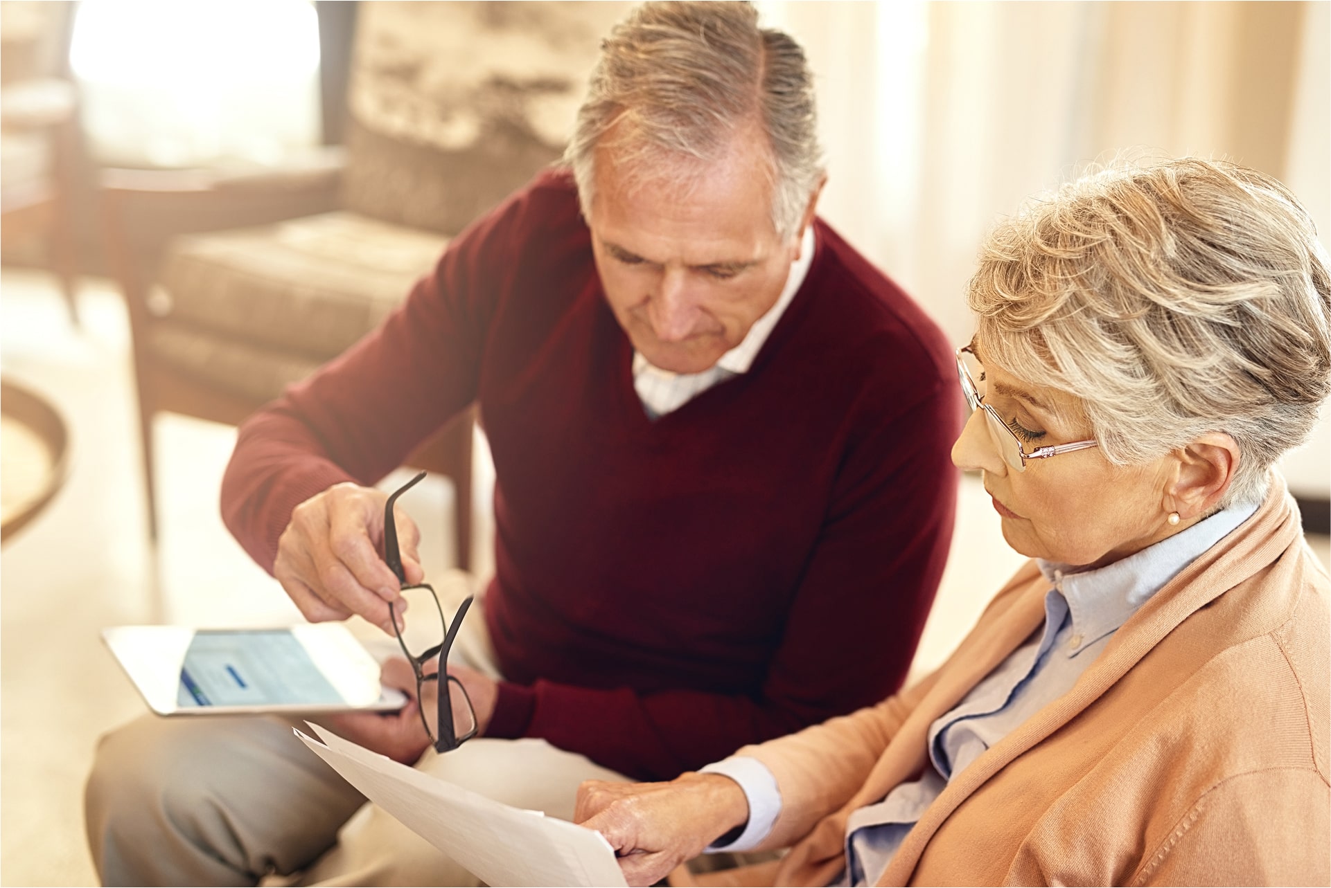 Senior couple reviewing documents together at home, with a tablet on the table.