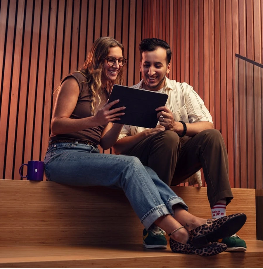 Lachende man en vrouw zitten op houten trappen en kijken samen naar een tablet.