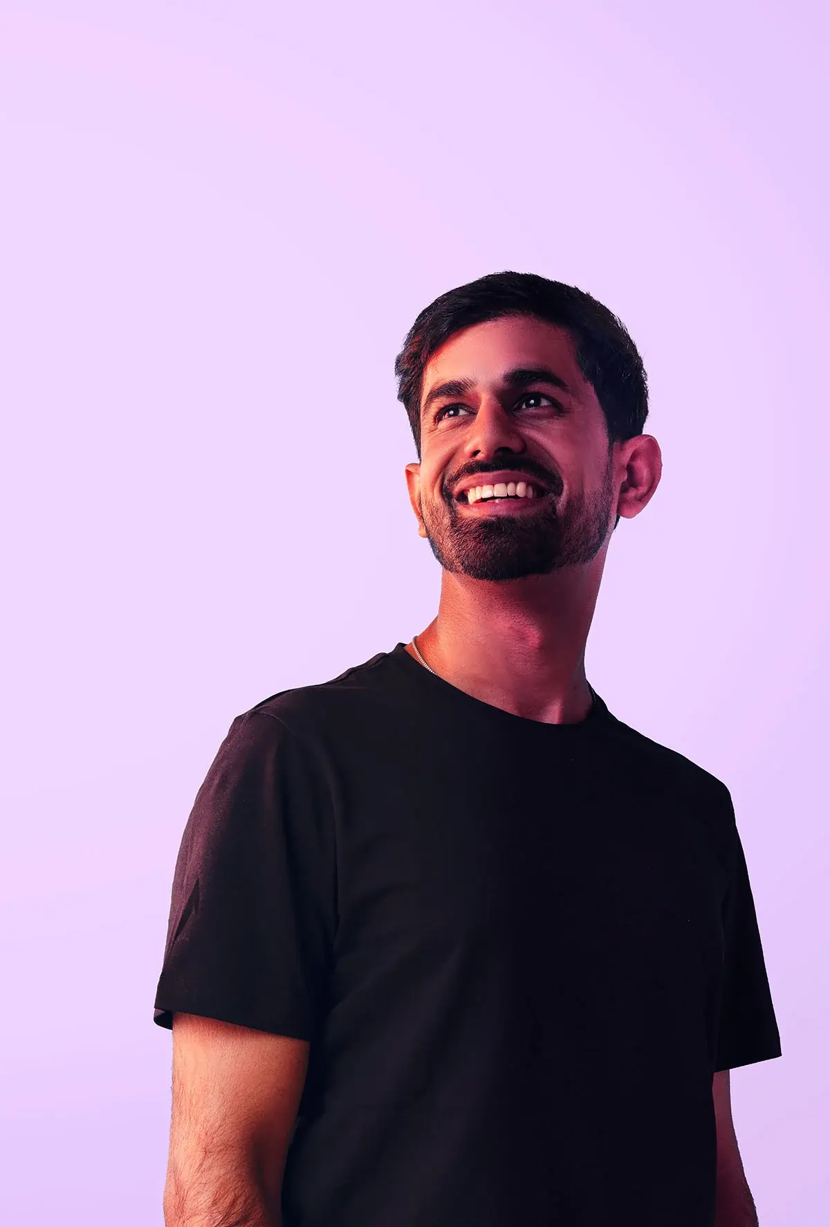 Person standing against a pastel purple background, wearing a plain dark t-shirt.