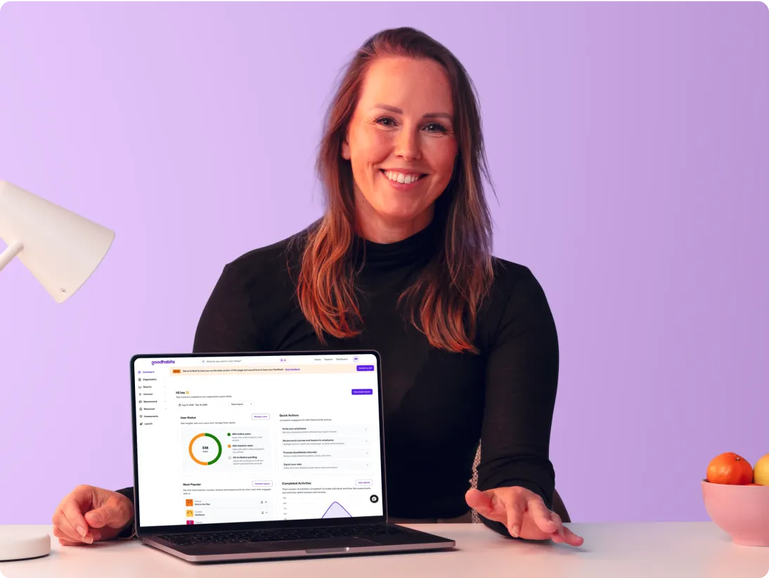 Friendly woman sitting at a desk showing the GoodHabitz dashboard on her laptop.