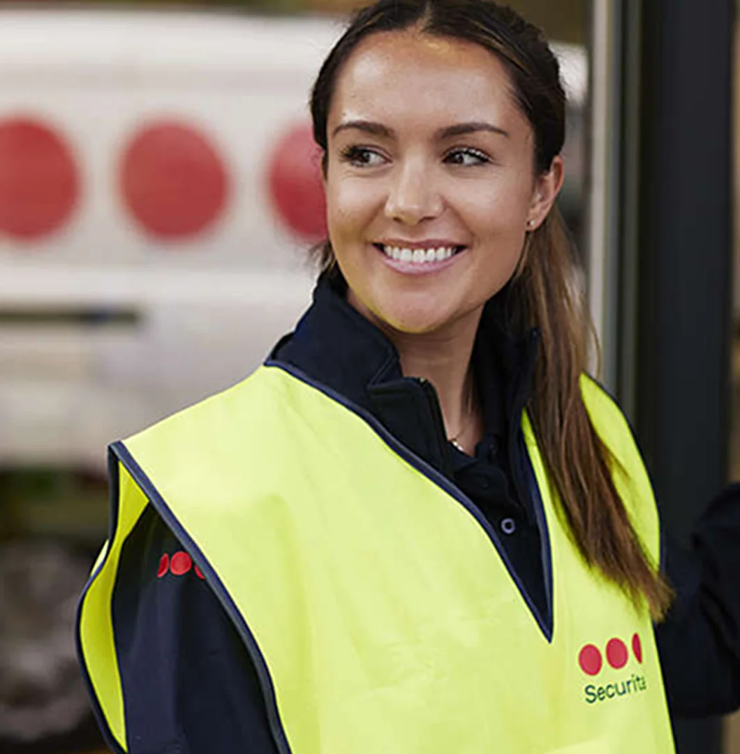 Close-up profile of a smiling woman looking to the side, wearing a yellow high-visibility vest with the Securitas logo.
