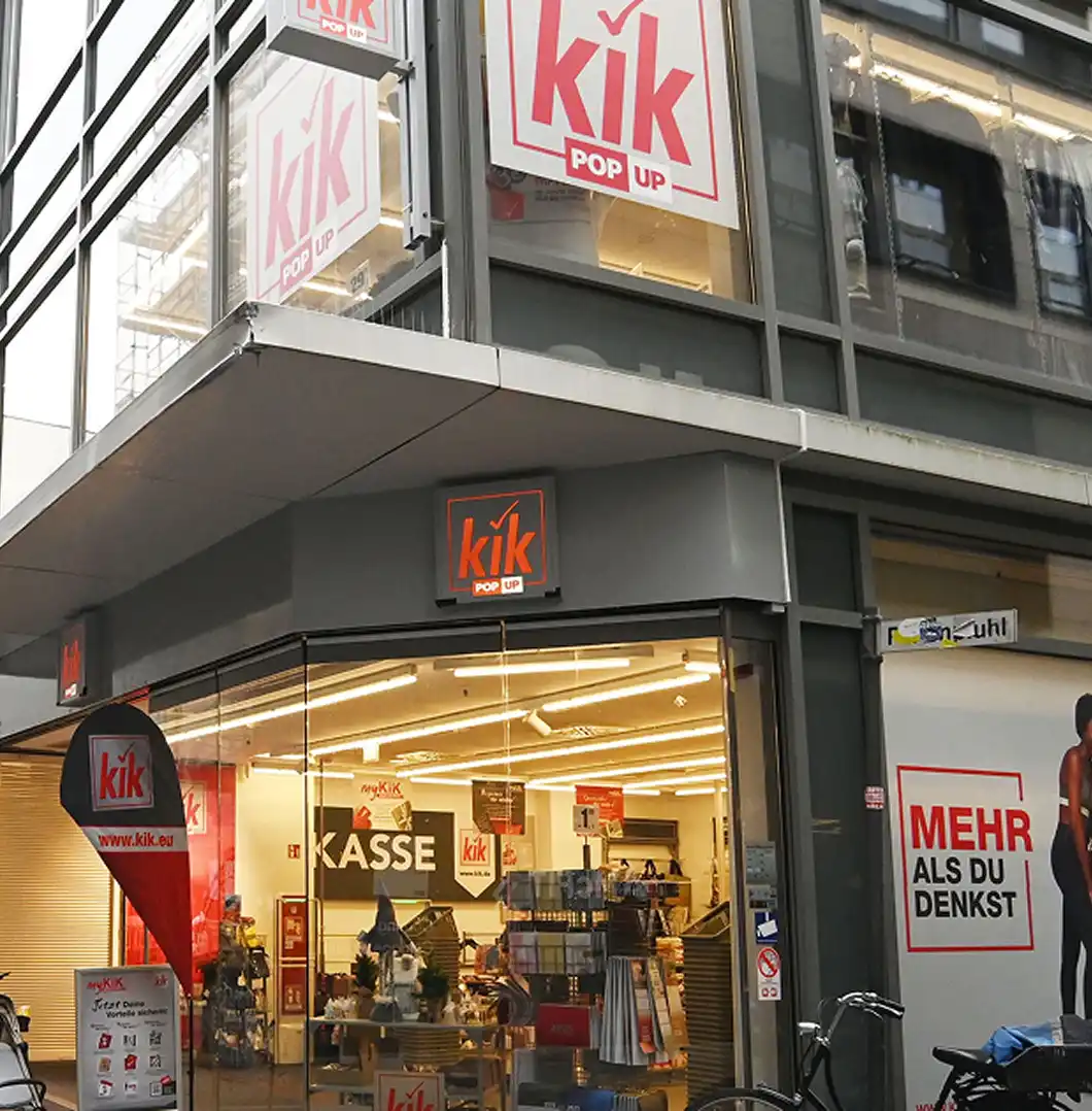 Exterior view looking up at the modern retail storefront and glass facade of a KiK POP UP store, with large branded signs displayed in the upper windows.