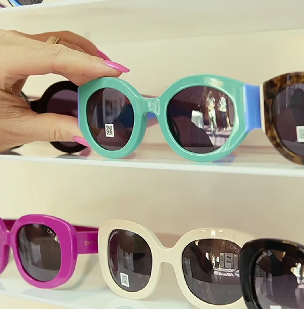 A hand adjusting a pair of chunky, mint-green round sunglasses on a retail display shelf.